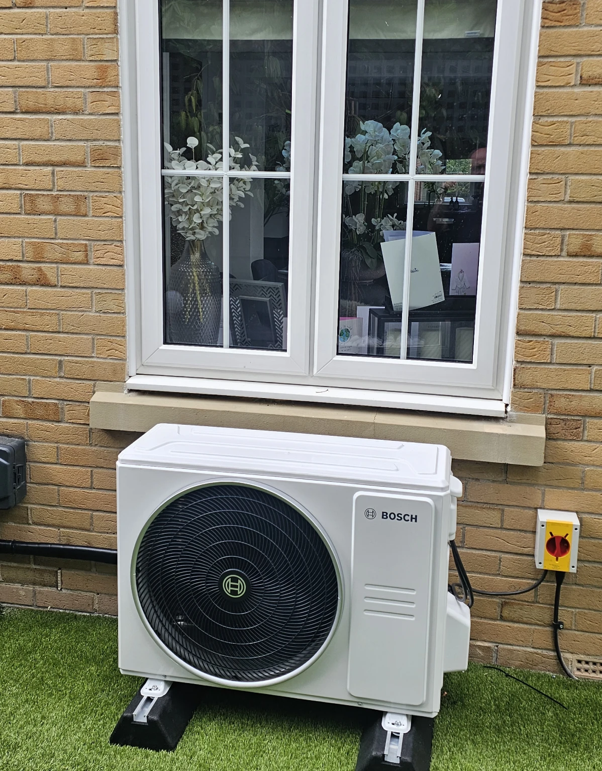 Bosch air conditioning outdoor unit on a lawn beneath a window